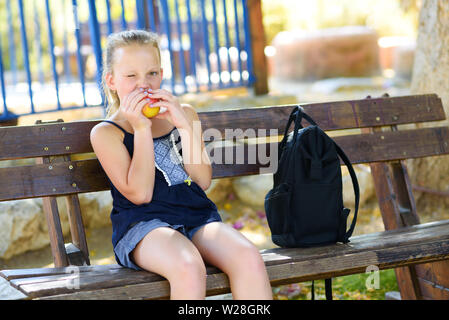 Kleines Mädchen isst einen Apfel. Gesunde Ernährung. Hübsches Kind Essen eines Apfels im Park, Natur. Jugendlicher Schüler genießen Sie gesundes Mittagessen im Schulhof. Stockfoto