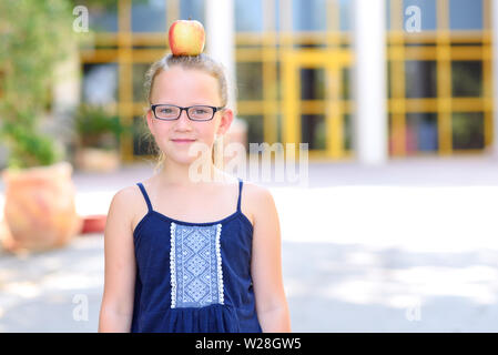 Happy girl In Gläsern mit Apfel auf den Kopf. Große Porträt der Schüler außerhalb des Unterrichts. Zurück zu Schule, Balance, Erfolg, Ziel und gesundes Essen für Kinder Konzept. Stockfoto