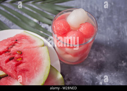Tropischer Obstsalat mit Melone und Wassermelone Kugeln aus Glas und palm leaf auf grauem Hintergrund Stockfoto