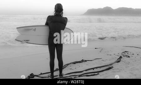 Ein Surfer im St James auf Gefahr Strand erwägt Rückkehr ins Meer, während eine andere Gruppe von Wellen auf Südafrikas Kap-halbinsel beobachten Stockfoto