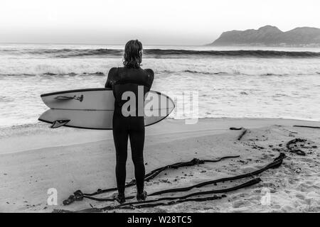 Ein Surfer im St James auf Gefahr Strand erwägt Rückkehr ins Meer, während eine andere Gruppe von Wellen auf Südafrikas Kap-halbinsel beobachten Stockfoto