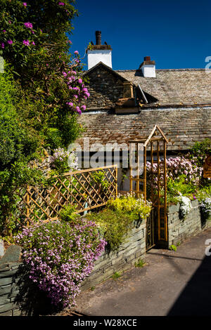 UK, Cumbria, Hawkshead, Wordsworth Street, kleine dreieckige Garten im Dorfzentrum mit Blumen Pflanzen auf Wand Stockfoto