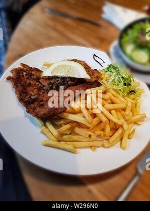 Wienerschnitzel, serviert mit Pommes Frites und Salat. Natürliche Holz Hintergrund. Vorderansicht Stockfoto