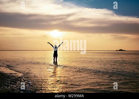 Ansicht der Rückseite des glücklichen Mann mit ausgestreckten Armen im Meer bei Sonnenuntergang. Stockfoto