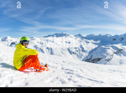 Bild von sportlichen Mann mit Helm tragen gelbe Jacke sitzen auf schneebedeckten Hang Stockfoto