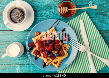 Selbstgemachte Waffeln mit Himbeeren und Blaubeeren, Tasse Kaffee, Milch und Besteck Stockfoto