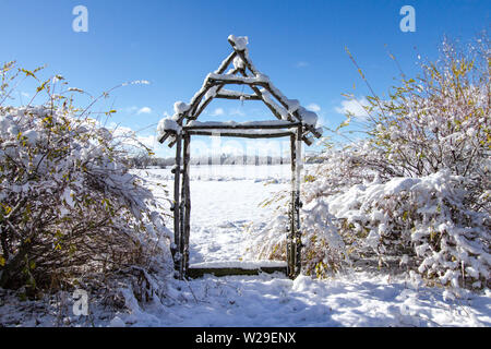 Winter Garten Landschaft. Rustikal Arbor von Pflanzen und Bäumen bedeckt unter einem frisch gefallenen Schnee Stockfoto