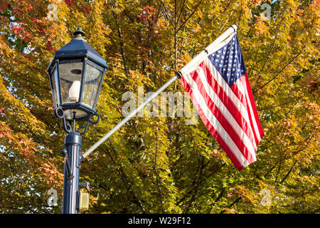 Small Town USA. Der Laternenpfosten der Main Street und die amerikanische Flagge werden im Mittleren Westen Amerikas gegen das wunderschöne Herbstlaub gerichtet. Stockfoto