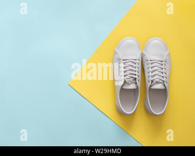 Weißes Leder Sneakers an blauen und gelben Hintergrund. Paar trendige Mode weißen Sport Schuhe oder Turnschuhe mit Kopie Platz für Text auf farbigen Hintergrund. Overhead shot der neuen weißen Turnschuhen. Flach Stockfoto