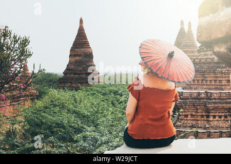 Kaukasische blonde Frau mit traditionellen burmesischen roten Regenschirm mit Blick auf Pagoden und Tempel der alten Bagan in Myanmar Stockfoto