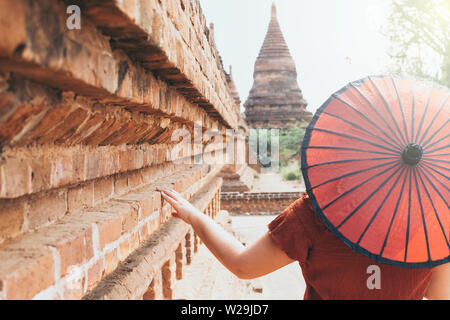 Frau mit traditionellen burmesischen roten Regenschirm mit Blick auf die Pagode und Tempel der alten Bagan in Myanmar Stockfoto