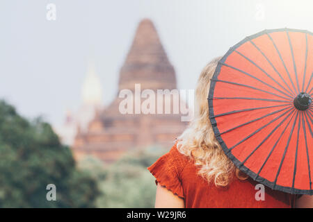 Blond kaukasische Frau mit roten traditionelle Dach schaut in Richtung Ananda Tempel und Pagoden von alten Bagan in Myanmar Stockfoto