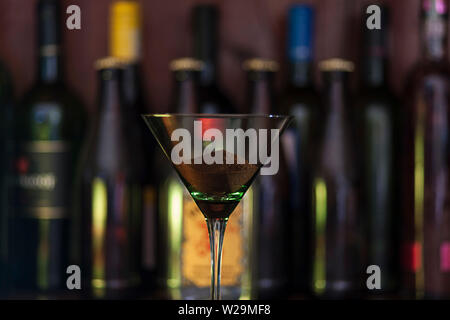 Close up Konzept Foto von Kaffeesatz in einem Cocktail Glas auf einen Tresen im schwachen Licht mit Alkohol Flaschen im Hintergrund. Stockfoto