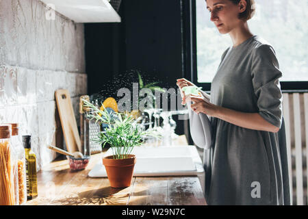 Junge Frau spritzt Wasser auf einer zimmerpflanze in der Küche, Slow Life Stockfoto