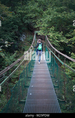 Zurück von einer jungen Frau auf Klastorna lavka Seil Fuß-Brücke über den Fluss Hornad, Slovensky Raj. Hohe dunkelgrünen Kiefern, warmen Tag im September. Konzept o Stockfoto