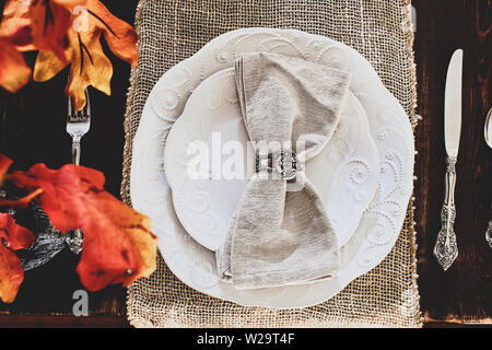 Thanksgiving Day oder Herbst Ort Einstellung mit Servietten und Besteck auf sackleinen Tischläufer über ein rustikales Bauernhaus Tabelle Hintergrund. Bunte fallen lassen Stockfoto