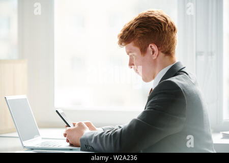 Junge Multitasking Geschäftsmann mit Smartphone vor Laptop Stockfoto