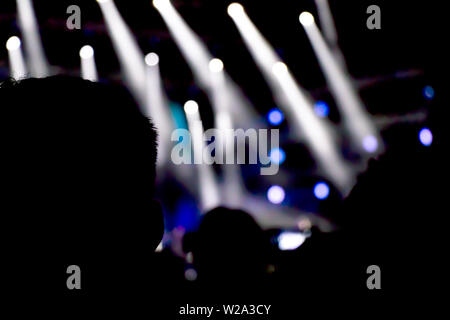 Silhouetten von Menschen beobachten das Konzert von hinten, mit Bühne Licht in der Ferne Stockfoto