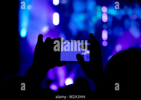 Das Sammeln digitaler Speicher verliert Fähigkeit, Gegenwart, Silhouette eines Mannes Hand schießen das Konzert mit seiner smart phone Stockfoto