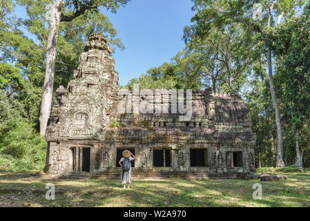 Eine touristische besuchen Angkor Ruinen inmitten Dschungel, Tempelanlage Angkor Wat, Reiseziel Kambodscha. Frau mit traditionellen Hut, Ansicht von hinten. Stockfoto