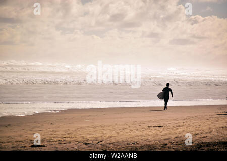 Surfer gehen hinunter Piha Strand bei Sonnenuntergang, Neuseeland Stockfoto