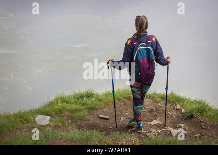 Ein Mädchen mit bunten Strumpfhosen, Rucksack und Wanderstöcke stehen am Rand des Sees Peak auf Rila-gebirge, berühmten Aussichtspunkt von Sieben Rila-Seen Stockfoto