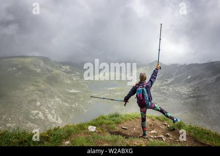 Ein Mädchen mit bunten Strumpfhosen, Rucksack und Wanderstöcke stehen am Rand des Sees Peak auf Rila-gebirge, berühmten Aussichtspunkt von Sieben Rila-Seen Stockfoto