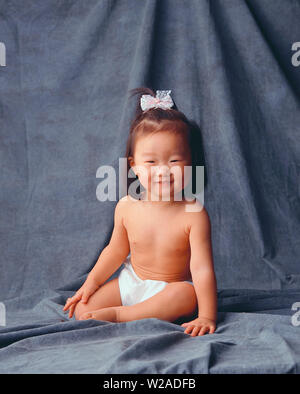 Asiatische Kleinkind sitzt auf einem grauen Hintergrund eine Windel tragen :-) Stockfoto