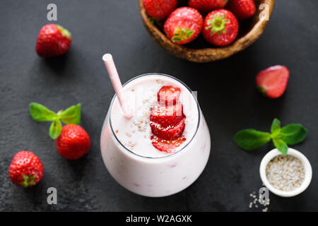 Strawberry Smoothie oder Milchshake in Glas mit Chia Samen und rosa Strohhalm auf schwarzem Hintergrund Stockfoto