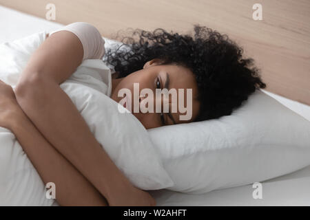 Traurig, deprimiert afrikanische Frau umarmen Kissen im Bett allein liegen Stockfoto