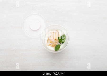 Joghurt birne Schichten und Minze und Pinienkernen liegen in einem Lunch Box auf einem weißen Tisch mit Pinienkernen und Birne Schichten, zerstreut werden. Gesunde Ernährung Konzept Stockfoto