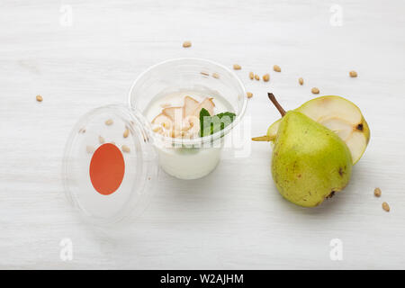 Joghurt birne Schichten und Minze und Pinienkernen liegen in einem Lunch Box auf einem weißen Tisch mit Pinienkernen und Birne Schichten, zerstreut werden. Gesunde Ernährung Konzept Stockfoto