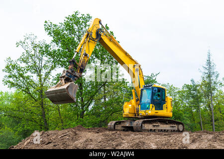 Gelber Gürtel von Bagger auf der Baustelle. Hydraulische earth Mover. Baggerlader. Rotierende Kabine, Schaufel und Continuous Track. Tree Top, Sky. Stockfoto