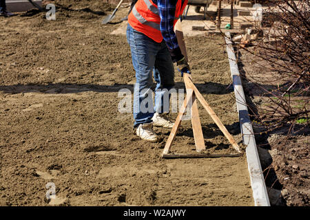 Der Arbeitnehmer richtet die Keller mit einem Holz- Ebene beginnen zu verlegen Pflastersteine auf die Fußgängerzone. Stockfoto