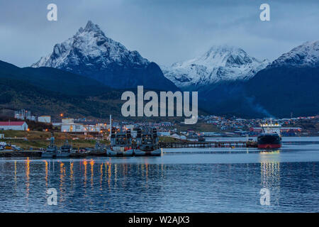 Schiff und Hafen Lichter reflektieren auf dem Wasser in den Hafen von Ushuaia gegen die kriegerische Bergkette Tierra del Fuego Argentinien in den frühen Abend. Stockfoto