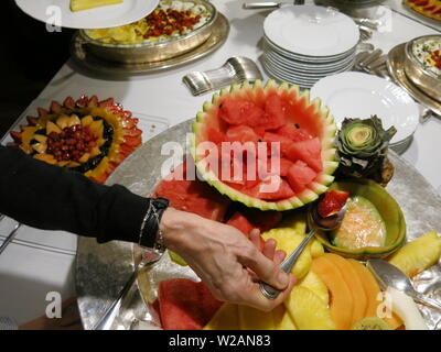 Die Hand einer Frau hält ein Löffel Erdbeeren aus einer Vielzahl von Desserts und Platten von frischem Obst, die den bei einem leckeren Buffet bedienen Stockfoto