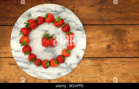 16 rote reife Erdbeeren in eine kreisförmige Form auf einem Marmor Rundschreiben Vorstand positioniert in der Mitte des Kreises der Erdbeeren ist eine große strawbe Stockfoto