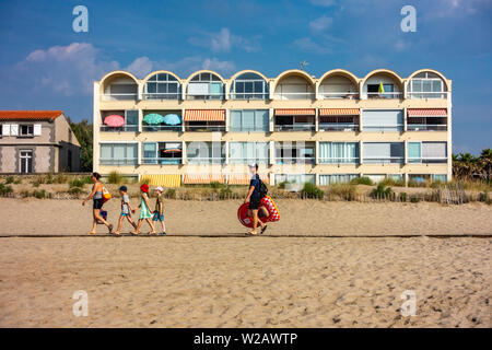 Familie zu Fuß entlang der Strandpromenade vor rund 1980's Holiday Apartments Stockfoto