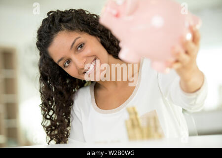 Fröhliche junge Frau mit sparschwein mit viel Geld Stockfoto