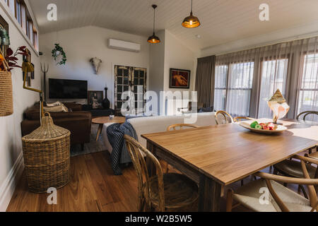 Ess- und Wohnbereich mit gewölbten Holz Öffnen gesäumt Decken und großen Fenstern mit Vorhängen und Bettwäsche Stockfoto
