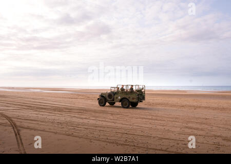 Vintage Weltkrieg 2 Jeep an einem Strand in der Normandie, Geländefahrten mit Menschen an Bord in den militärischen Uniformen Stockfoto