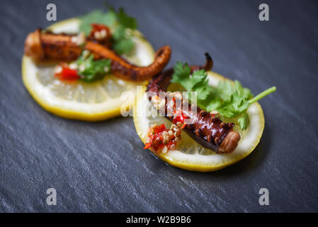 Oktopus Salat auf Zitrone Kräuter und Gewürze auf dunklen Platte/Tentakel Tintenfisch gegrillt Vorspeise essen heiß und würzig Chili Sauce gekocht serviert Meeresfrüchte Stockfoto