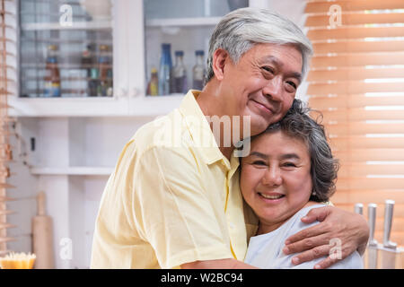 Asiatische senior Paar togerther Umarmen und an Kamera und in der Küche zu Hause lächelnd. Happy Aging zu Hause Konzept Stockfoto