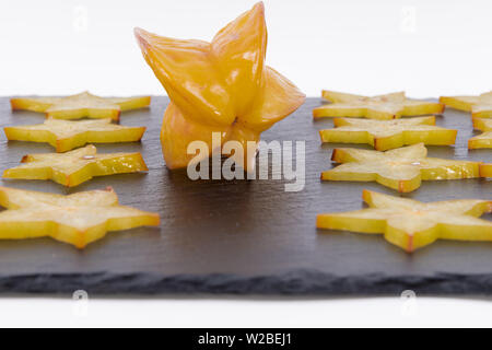 Averrhoa carambola - in Scheiben geschnitten und ganze tropische carambolas - frisch und reif stafruit auf einem schwarzen Brett - auf weißem Hintergrund Stockfoto