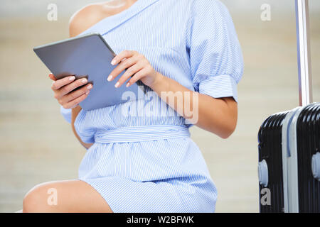 Zugeschnittenes Bild der jungen Frau an Koffer im Freien sitzen und lesen Artikel auf Tablet-PC Stockfoto