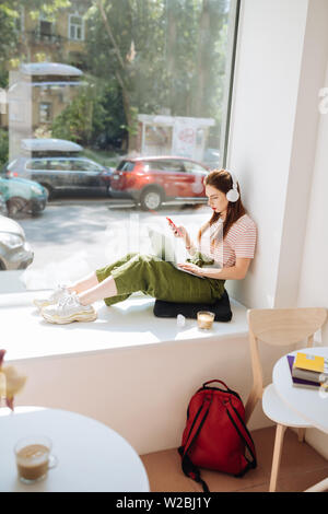 Das Abrufen von E-Mails. Schöne junge Frau sitzt auf der Fensterbank und auf dem Bildschirm ihres Laptops Stockfoto