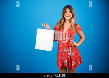 Porträt der Schönen lächelnden jungen Frau im roten Kleid mit Blumenmuster, Shopping Bag von Fashion Boutique Stockfoto