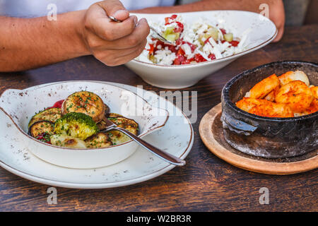 Die nationalen Montenegrinischen essen. Salziger Pfannkuchen mit Fleisch und Käse in einer gusseisernen Topf, gebackenem Gemüse und Salat auf den Tisch im Restaurant. Stockfoto