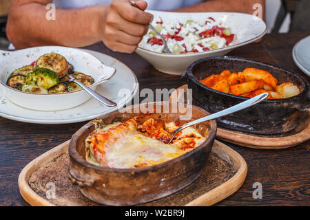 Die nationalen Montenegrinischen essen. Salziger Pfannkuchen mit Fleisch und Käse in einer gusseisernen Topf, gebackenem Gemüse und Salat auf den Tisch im Restaurant. Stockfoto