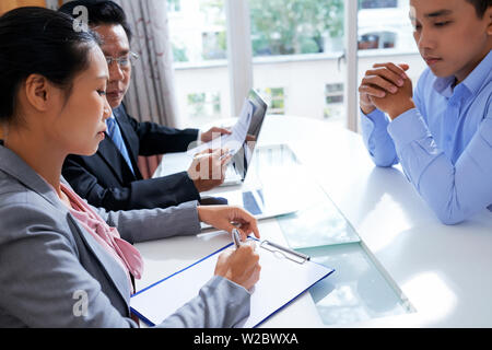 Reifen asiatischen menschlichen Ressourcen ermöglichen, Manager lesen Lebenslauf als seine weiblichen Kollegen, sich Notizen während der Job Interview mit jungen Antragsteller Stockfoto
